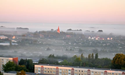 Dörp Lichtenhagen in'n Morgennäbel. De Stadt Rostock is dicht ranrückt